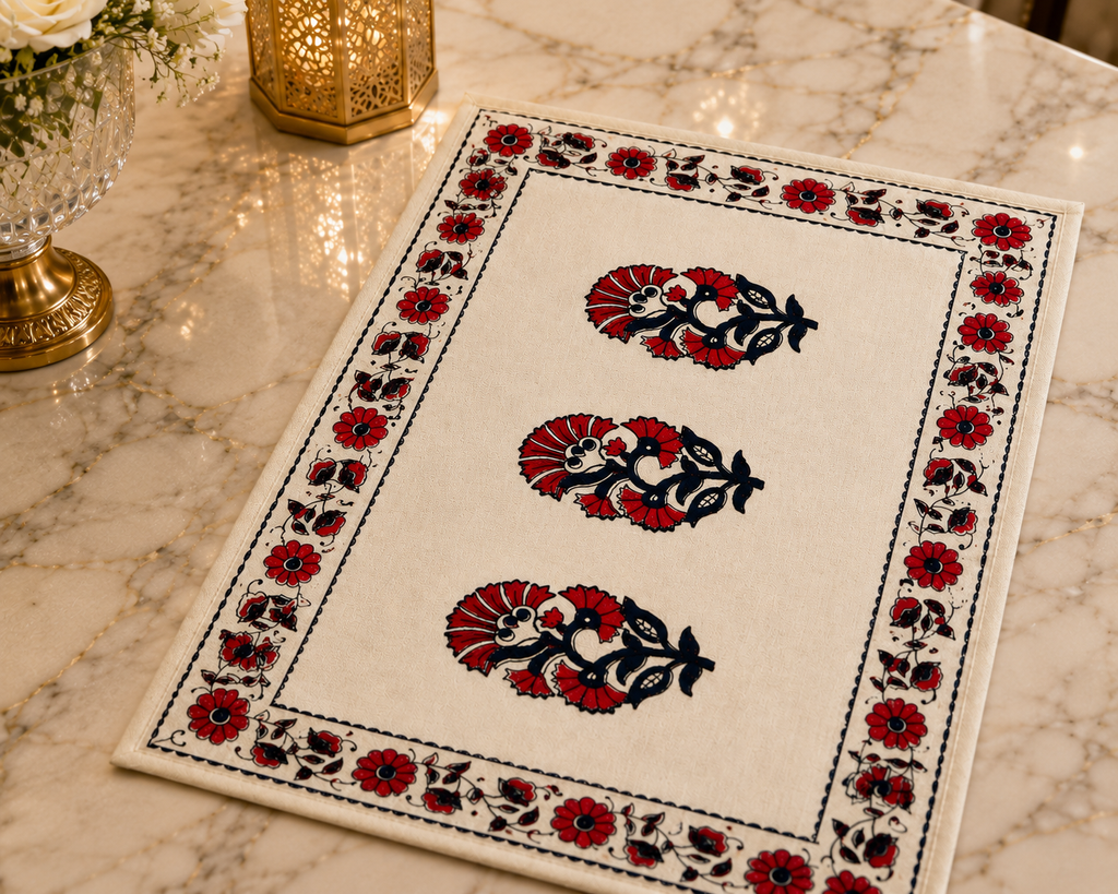 A rectangular cream-colored table mat with a black and red floral block print design, styled on a polished marble tabletop next to a gold lantern and a glass vase.